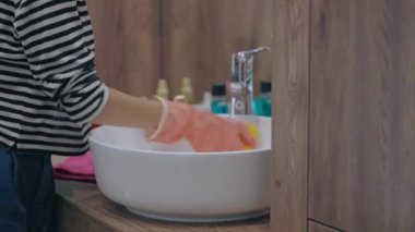 Lastik eldivenli, banyo lavabosunu temizleyen genç bir kadın.