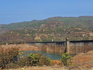 Dağ barajı manzarası. Yeşil tepeler ve parlak güneş ışığı altındaki kuru bitki örtüsüyle çevrili geniş bir baraj manzarası. Engebeli arazide doğal mühendisliği yakalıyor..