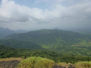 Bulutlu gökyüzünün altındaki yemyeşil tepelerin ve vadilerin geniş manzarası Matheran tepe istasyonunun doğal güzelliğini ve manzarasını gözler önüne seriyor..