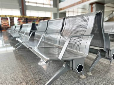 Modern havaalanındaki boş metal koltuklar parlak doğal ışık parlayan zemine yansıyor. Sakin atmosfer, toplu taşıma ve şehir tasarımını gösteren minimalist seyahat kavramı