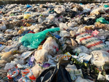 Plastik kirliliği, çevresel hasarı, atık yönetimi sorunlarını, geri dönüşüm krizini, sürdürülebilirlik sorunlarını ve küresel çevre bilincini vurgulayan açık bir çöplükte büyük miktarda plastik atık ve çöp torbası yığını