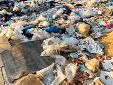Plastik kirliliği, çevresel hasarı, atık yönetimi sorunlarını, geri dönüşüm krizini, sürdürülebilirlik sorunlarını ve küresel çevre bilincini vurgulayan açık bir çöplükte büyük miktarda plastik atık ve çöp torbası yığını