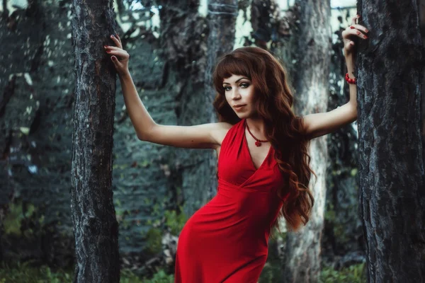 Dívka s dlouhé a vlnité vlasy v červených šatech v lese — Stock fotografie