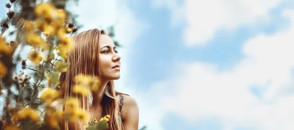 Schönes, natürliches Mädchen zwischen gelben Blumen und Wolken blickt in die Ferne. Großes Banner. — Stockfoto