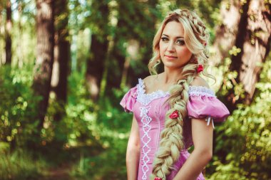 Beautiful girl with a long braid in pink lace dress smiles in the forest. clipart