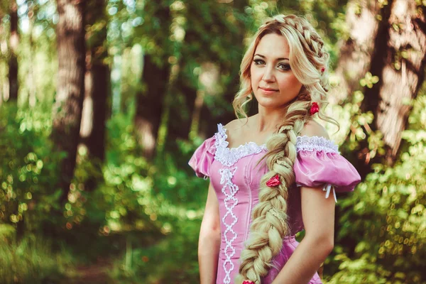 Menina bonita com uma longa trança no vestido de renda rosa sorrisos na floresta . — Fotografia de Stock