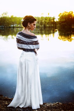 Kız bir nehir kenarında günbatımında duruyor.