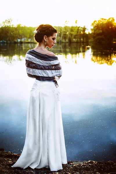 Kız bir nehir kenarında günbatımında duruyor.