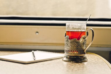 Trendeki bardak tutacağındaki çay masanın üzerinde, bir not defterinin yanında.