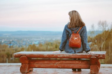Kız bankta oturur ve uzaklara bakar.