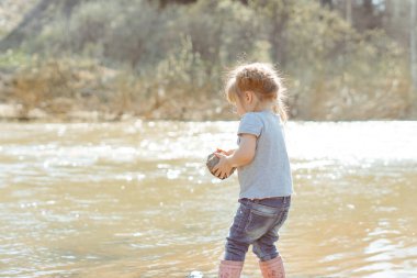 Küçük kız nehir kenarında kayalarla oynuyor.
