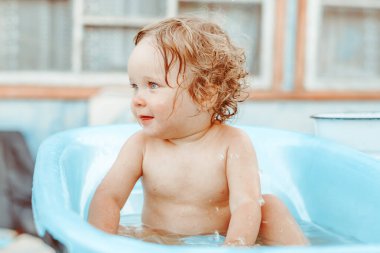 Küçük bir çocuk bir köy evinin yakınındaki sokakta banyo yapıyor.