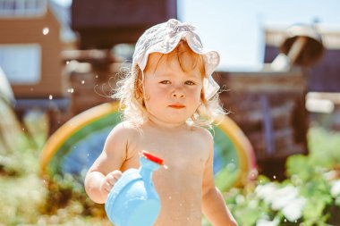 Bir çocuk güneşli bir günde bahçede bir su bidonuyla oynar.