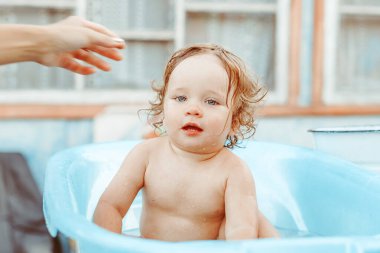 Küçük bir çocuk bir köy evinin yakınındaki sokakta banyo yapıyor.