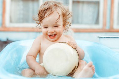 Küçük bir çocuk bir köy evinin yakınındaki sokakta banyo yapıyor.