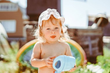Bir çocuk güneşli bir günde bahçede bir su bidonuyla oynar.