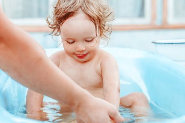 Küçük bir çocuk bir köy evinin yakınındaki sokakta banyo yapıyor.