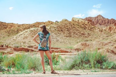 Ayakta duran kız, dağların arasındaki asfalt yola sırtını döndü.