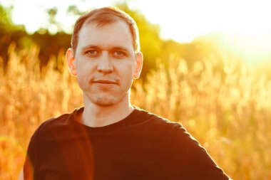 Gün batımında çimlerin üzerinde siyah tişörtlü bir adam.