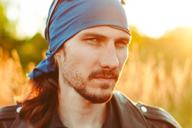 Siyah deri ceketli bir adam gün batımında çimlerin üzerinde