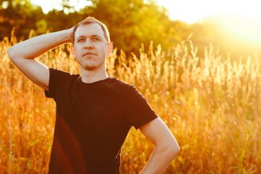 Gün batımında çimlerin üzerinde siyah tişörtlü bir adam.