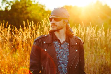 Siyah deri ceketli bir adam gün batımında çimlerin üzerinde