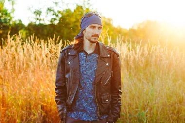 Siyah deri ceketli bir adam gün batımında çimlerin üzerinde