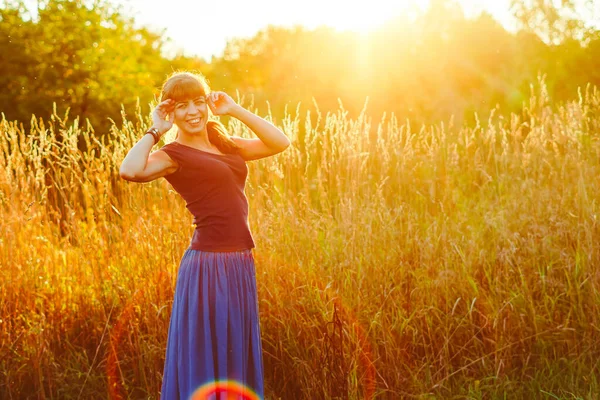 Buğday tarlasında duran genç bir kadın ve arka planda gün doğumu