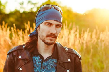 Siyah deri ceketli bir adam gün batımında çimlerin üzerinde
