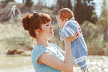 Bir anne çocuğu kollarında tutar nehrin kenarında durur.