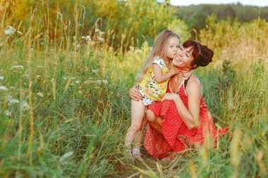 Anne çocuklarla çimenlerde oturuyor.