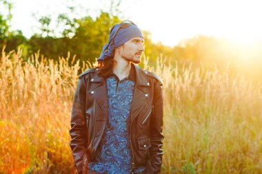 Siyah deri ceketli bir adam gün batımında çimlerin üzerinde