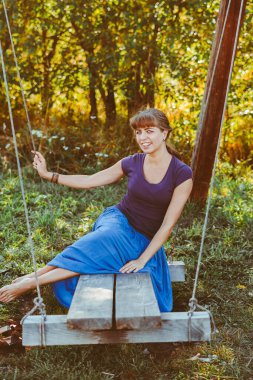 Beyaz gelinlik içinde, ormanda gülümseyen ve sallanan güzel bir gelinin portresi.