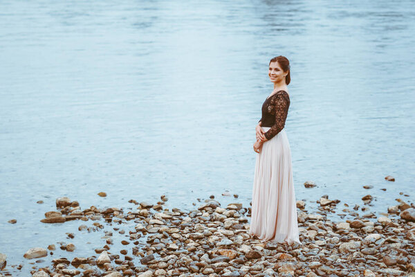 Beautiful girl in a dress by the river in cloudy weather