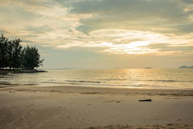 Gün batımında sakin tropikal bir sahil. Kuma ve sakin okyanus dalgalarına yansıyan yumuşak altın bir ışık.