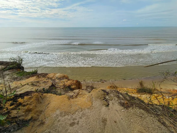 Tusan Sahili 'nde bulutlu bir gökyüzünün altındaki okyanus dalgalarına bakan kumlu bir uçurumdan yüksek açılı bir manzara. Tusan Sahili, Miri, Sarawak, Borneo, Malezya