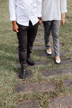 Ahşap bahçe yolunda yürüyen, şık giyinmiş genç bir çiftin alt kesim manzarası.