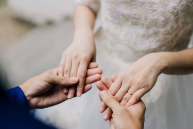 Bir damat gelinin elini nazikçe tutar, parmağındaki altın alyansı dantelli gelinliğine vurgular..