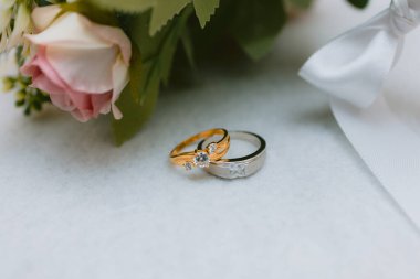 Bir çift alyansın yakın plan fotoğrafı. Üç elmas ve bir gümüş yüzük. Pembe bir buketin yanına yerleştirilmiş.