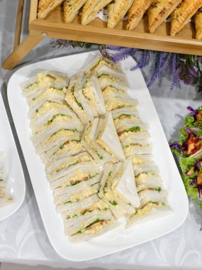 Tertemiz hazırlanmış yumurtalı mayonezli sandviçlerle dolu beyaz bir tabak..