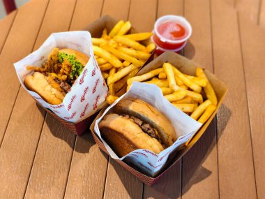 Büyük porsiyonlarda altın patates kızartması ve ahşap bir masanın üzerinde kırmızı biber sosuyla servis edilen markalı kâğıt ambalajlı iki gurme sığır burger. 2 Temmuz 2025, Kuching, Sarawak, Malezya