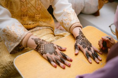 Geleneksel kına (mehndi) tasarımları, altın başlıklı geleneksel Malay elbisesiyle bir gelinin ellerinde..