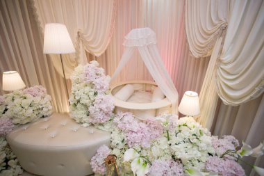 Yuvarlak Bebek Beşiği ve Çiçek Dekoru 'nun yakın çekimi. Yumuşak pembe ve beyaz ortancalar ve zarif beyaz perdelerle çevrili beyaz dairesel bebek beşiğinin yukarıdan aşağı perdesi..