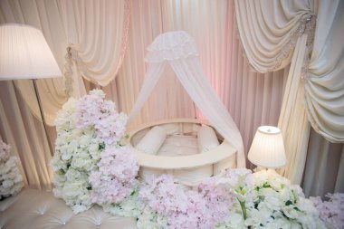 Ilık Işıklı Bebek İsimlendirme Seremonisi Detaylı Görünümü. Beyaz bir beşik, zemin lambaları ve tarafsız renklerde kumaşların yer aldığı bir bebek kutlaması sahnesine samimi bir bakış..