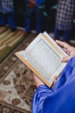 İslam ayini sırasında Kur 'an okuyan kişi. Geleneksel Arapça kaligrafi içeren kutsal Kur 'an' ı dinsel bir toplantı ya da namaz oturumunda tutan ellerin yakın çekimi..