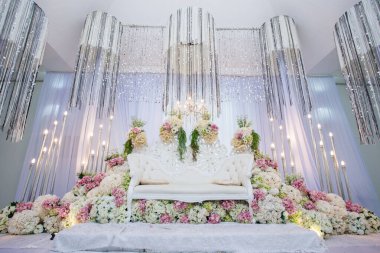 Lüks Beyaz Çiçekli Düğün Sahnesi Tasarımı. Süslü beyaz bir kanepe, büyük bir çiçek aranjmanı ve kristal ışıklı eşyalar içeren büyük bir düğün kürsüsü veya 