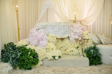 Beyaz Wicker Baby Bassinet ve çiçek yayası. Modern altın geometrik zemin lambalarıyla çevrili, bir krema ve pembe güllerden oluşan bir yatağın üzerine yerleştirilmiş lüks bir beyaz hasır..