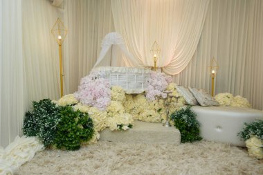 Beyaz Wicker Baby Bassinet ve çiçek yayası. Modern altın geometrik zemin lambalarıyla çevrili, bir krema ve pembe güllerden oluşan bir yatağın üzerine yerleştirilmiş lüks bir beyaz hasır..