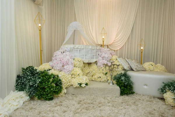 Beyaz Wicker Baby Bassinet ve çiçek yayası. Modern altın geometrik zemin lambalarıyla çevrili, bir krema ve pembe güllerden oluşan bir yatağın üzerine yerleştirilmiş lüks bir beyaz hasır..