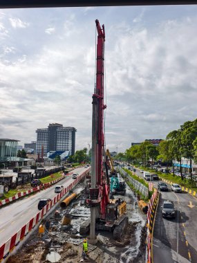 Trafiğin ortasında bir altyapı projesi için derin temeller hazırlayan uzun kırmızı bir sondaj makinesi şehrin inşaat bölgesinde belirgin bir şekilde duruyor. 5 Şubat 2026, Kuching, Sarawak, Malezya.